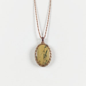 Op de afbeelding: Een ketting van bruin koord met een ronde hanger van gele en groene steen.