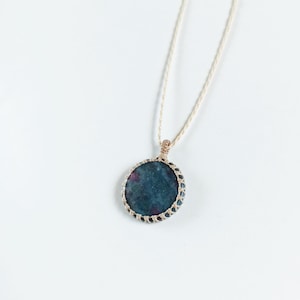 May include: A dark green and pink gemstone pendant necklace with a woven cord. The pendant is round and has a delicate wire frame.