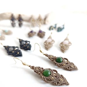 Puede incluir: Un par de pendientes de macramé marrones con cuentas de piedras preciosas verdes. Los pendientes tienen forma de diamante y tienen detalles dorados.