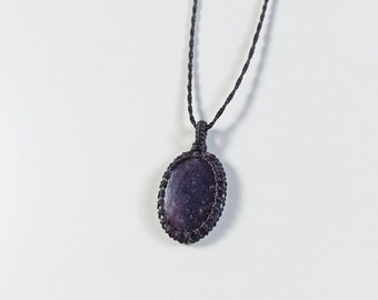 May include: A handcrafted necklace featuring a dark purple, oval-shaped stone pendant. The stone is encased in a woven, dark-colored macrame setting and hangs from a matching cord. The pendant is approximately 1 inch in length.