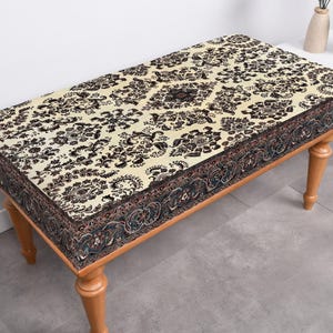 May include: A wooden bench with a cream and brown patterned cushion. The cushion has a dark brown border with a floral design.