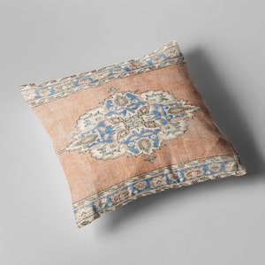 May include: A decorative pillow with a peach-colored background and a blue and white floral pattern. The pillow has a fringed border.
