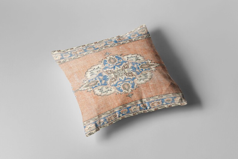 May include: A decorative pillow with a peach-colored background and a blue and white floral pattern. The pillow has a fringed border.
