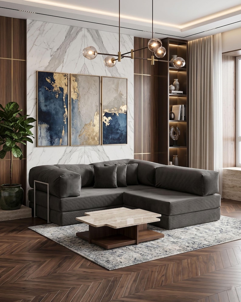 May include: A modern living room featuring a dark gray sectional sofa, a marble-topped coffee table, and abstract art with gold accents. The room has a hardwood floor and a patterned rug. Decorative lighting hangs from the ceiling.