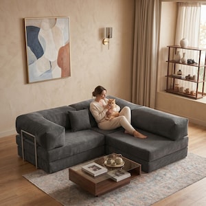 May include: A modern, gray sectional sofa with a corduroy texture. The sofa has a low profile and is paired with a wooden coffee table with a glass top. A decorative painting hangs on the wall, and a rug is on the floor.