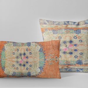 May include: Two decorative throw pillows with a vintage rug pattern. The pillows are rectangular and feature a colorful design with shades of orange, blue, green, and pink. The pattern is intricate and includes floral motifs and geometric shapes.