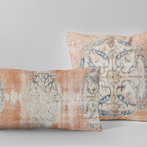 May include: Two decorative throw pillows with a distressed, vintage rug design. The pillows feature a peach-colored background with intricate blue and cream-colored patterns. One pillow is rectangular, the other square.