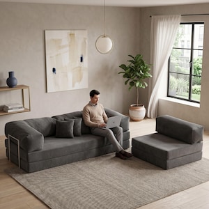 May include: A modern gray modular sofa and matching armchair set. The sofa has a low profile with square cushions and metal accents. The armchair is a single-seat version. The set is placed on a patterned rug in a neutral-toned living room.