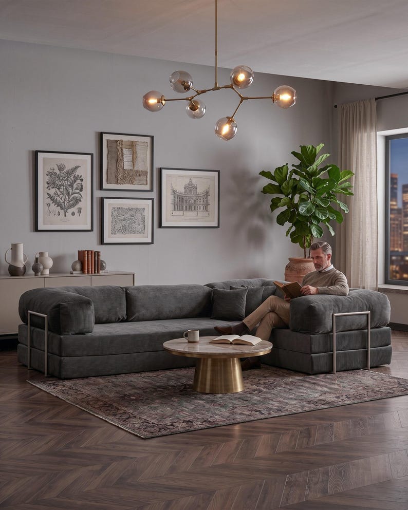 Puede incluir: Un sal&oacute;n moderno con un gran sof&aacute; seccional gris oscuro con detalles met&aacute;licos. Una mesa de centro redonda con tapa de m&aacute;rmol y base dorada descansa sobre una alfombra estampada. Obras de arte cuelgan de la pared gris y una l&aacute;mpara decorativa cuelga del techo.