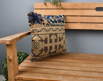 Könnte beinhalten: Ein farbenfrohes, gemustertes Kissen mit geometrischem Design in Blautönen, Grün, Braun und Beige. Das Kissen liegt auf einer Holzbank.