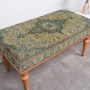 May include: A wooden bench with a patterned fabric seat. The fabric has a green, blue, and beige colour scheme with a floral design.