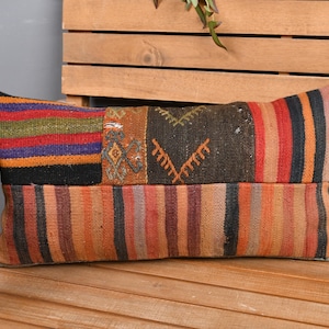 May include: Rectangular decorative pillow with a patchwork design. The pillow features a mix of colors including orange, red, green, and black. The pillow is placed on a wooden bench.