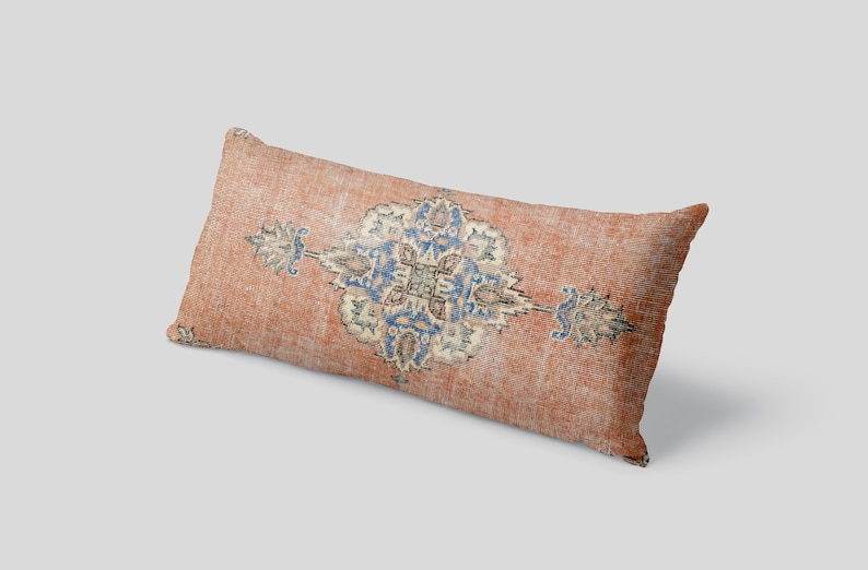 May include: A long, rectangular pillow with a peach-colored fabric featuring a blue and cream-colored geometric pattern.