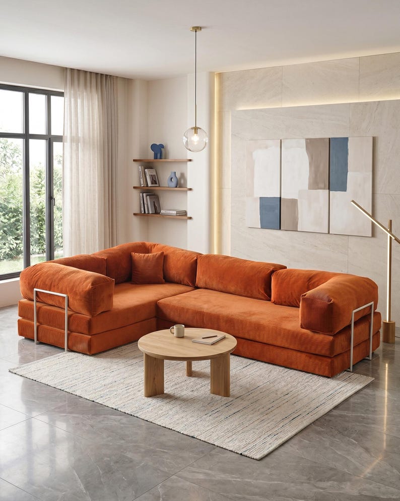 Puede incluir: Un sof&aacute; seccional naranja con detalles met&aacute;licos. Una mesa de centro redonda de madera descansa sobre una alfombra crema. La habitaci&oacute;n tiene un dise&ntilde;o moderno, una ventana grande y obras de arte abstractas.