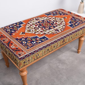 May include: A wooden bench with a colorful patterned cushion. The cushion features a traditional rug design with orange, blue, and white colors.