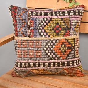 May include: A square, patterned pillow with a woven texture. The pillow features a patchwork design with a mix of colors including orange, purple, yellow, and black. The pillow is resting on a wooden chair.