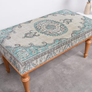 May include: A wooden bench with a light blue and beige patterned cushion. The cushion has a floral design with a central medallion.