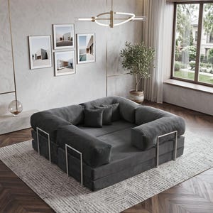Puede incluir: Un sof&aacute; modular gris oscuro con un perfil bajo y reposabrazos redondeados. El sof&aacute; est&aacute; sobre una alfombra estampada y tiene soportes de metal plateado. Cojines decorativos y obras de arte enmarcadas completan el ambiente.