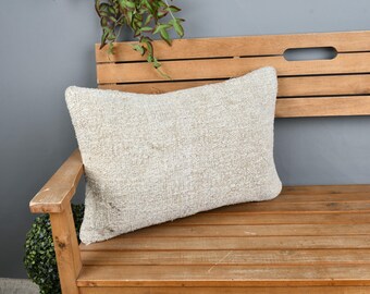 May include: A light gray throw pillow with a textured surface sits on a wooden bench. The bench has a slatted back and a natural wood finish.