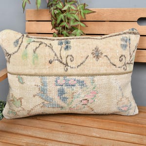 May include: A beige throw pillow with a floral pattern in shades of blue, pink, and green. The pillow is made of a soft, woven fabric and has a subtle distressed look.