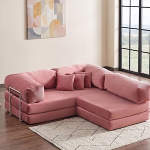 May include: A modular, sectional sofa in a dusty rose color. The sofa has a corduroy texture and includes several matching throw pillows. A metal frame supports the armrest. The sofa sits on a cream-colored rug with a geometric pattern.
