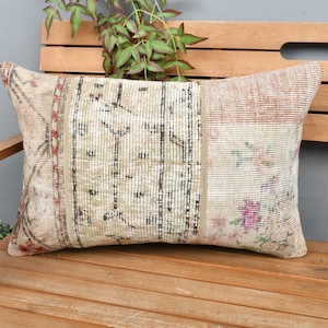 Puede incluir: Una almohada decorativa con un diseño de patchwork que presenta un fondo beige con motivos florales marrones, rojos y rosas. La almohada está hecha de una tela suave y tejida y tiene una forma rectangular.