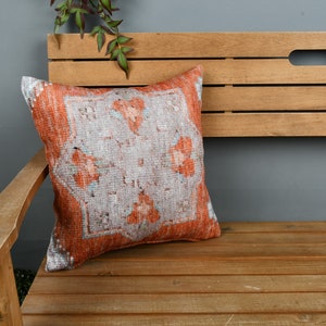 May include: A wooden bench with a decorative orange and white patterned throw pillow. The bench has a slatted back and armrests.