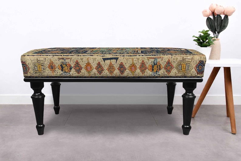 May include: A rectangular bench with a patterned cushion in beige, orange, and blue hues. The bench has a black frame and four turned legs. The cushion design has a vintage, rug-like appearance.