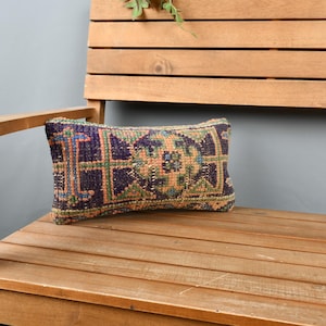 May include: A colorful patterned throw pillow with a geometric design in shades of blue, green, orange, and brown. The pillow is sitting on a wooden bench.