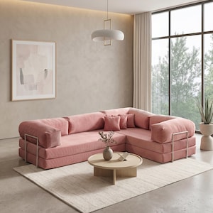 Puede incluir: Un gran sof&aacute; esquinero rosa con textura de pana y detalles met&aacute;licos. Una mesa de centro redonda de madera descansa sobre una alfombra crema. La habitaci&oacute;n cuenta con una obra de arte abstracta enmarcada y una moderna l&aacute;mpara colgante.