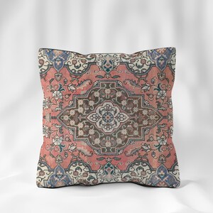 Può includere: Cuscino quadrato con design a tappeto vintage. Il cuscino presenta un medaglione centrale nei toni del marrone, circondato da uno sfondo corallo con motivi floreali e a volute. Accenti blu e bianchi completano il design.