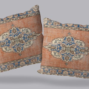 May include: Two decorative throw pillows with a vintage rug design. The pillows feature a central medallion in shades of blue, beige, and cream on a peach-colored background. The border is a repeating pattern of blue, beige, and cream.