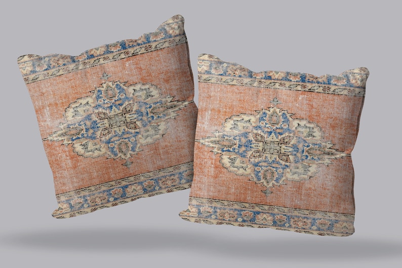 May include: Two decorative throw pillows with a vintage rug design. The pillows feature a central medallion in shades of blue, beige, and cream on a peach-colored background. The border is a repeating pattern of blue, beige, and cream.