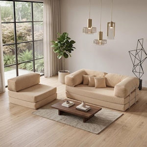 May include: A modern living room setup featuring a beige sofa, armchair, and a low wooden coffee table. The room is illuminated by pendant lights and natural light from a large window. A potted plant and decorative sculpture add to the decor.