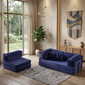 May include: A modern living room setup featuring a navy blue modular sofa and armchair. A patterned rug sits on the wooden floor. A large window with sheer curtains and a decorative wall hanging complete the scene. A potted plant adds a touch of nature.