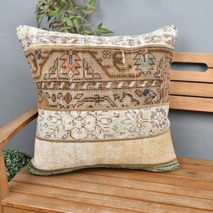 May include: A decorative pillow with a beige and brown patterned fabric. The pillow is sitting on a wooden bench.