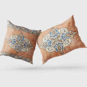 May include: Two decorative throw pillows with a vintage, faded look. The pillows feature a traditional Persian rug design in shades of orange, blue, and white.