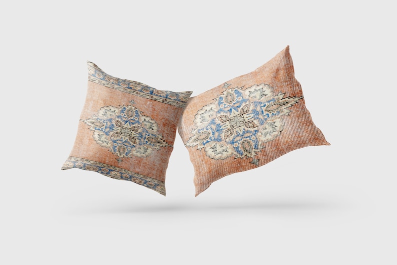 May include: Two decorative throw pillows with a vintage, faded look. The pillows feature a traditional Persian rug design in shades of orange, blue, and white.