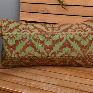 May include: A rectangular cushion with a green and brown floral design. The cushion is placed on a wooden bench. The design features a repeating pattern of stylized flowers and leaves. The cushion is approximately 40 cm long.