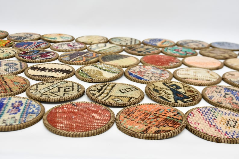 May include: A set of 20 round coasters made from colourful patterned fabric with a brown woven trim. The coasters are arranged in a semi-circle pattern on a white surface.