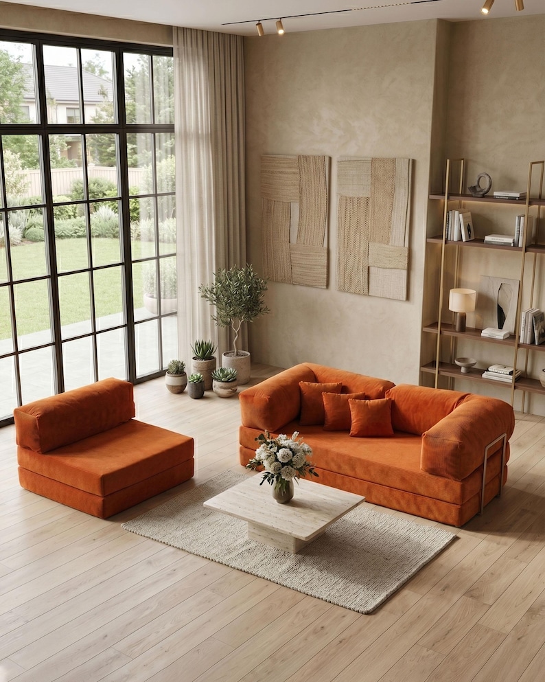 May include: An orange modular sofa and matching armchair set in a modern living room. The sofa has several orange throw pillows and sits on a light-colored rug. A square marble coffee table holds a vase of flowers.