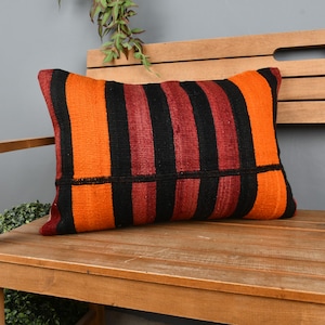 May include: A striped throw pillow with orange, black, and burgundy stripes. The pillow is sitting on a wooden bench.