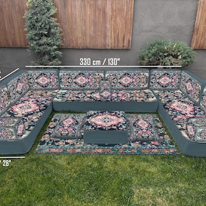 Puede incluir: Un conjunto de asientos para exteriores en forma de U con una alfombra y cojines estampados. El conjunto mide 330 cm de ancho, 190 cm de profundidad y 70 cm de alto. Los cojines y la alfombra presentan un diseño floral con acentos rosas, azules y verdes.