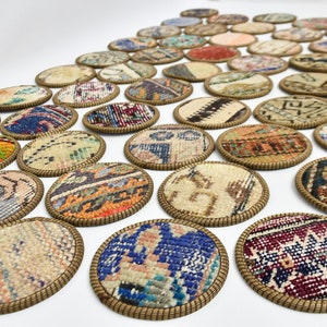 May include: A set of round coasters featuring colourful, intricate patterns woven into the fabric. The coasters are edged with a gold-coloured trim.