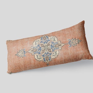 May include: A long, rectangular pillow with a faded, orange-brown fabric. The pillow features a blue and white floral pattern in the center.