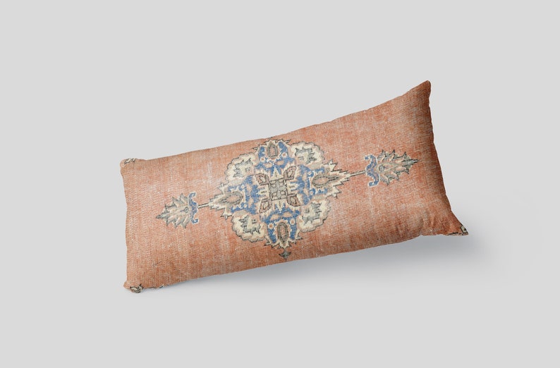 May include: A long, rectangular pillow with a faded, orange-brown fabric. The pillow features a blue and white floral pattern in the center.