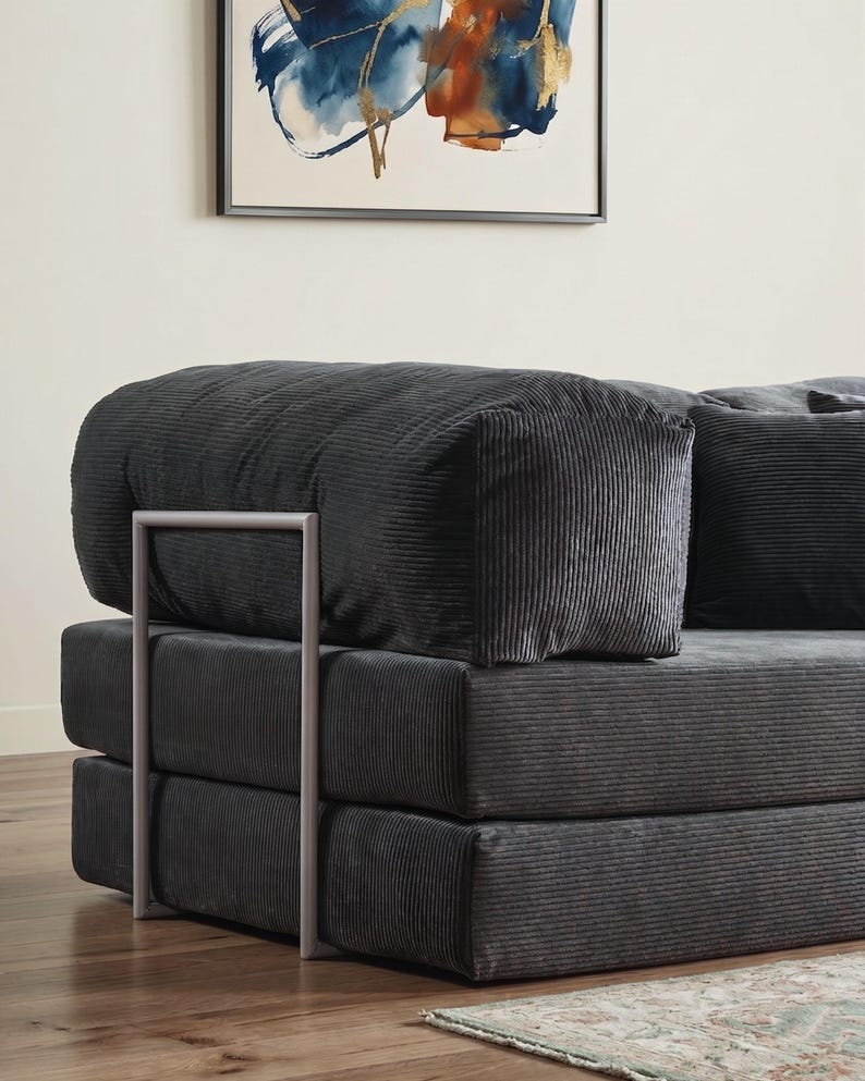 Puede incluir: Un sof&aacute; modular de pana gris antracita con una estructura met&aacute;lica minimalista. El sof&aacute; presenta un dise&ntilde;o apilado con secciones gruesas y acolchadas y un reposabrazos redondeado. La tela de pana tiene una textura acanalada vertical.