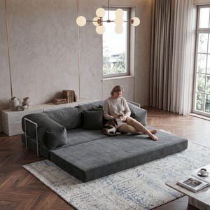 Puede incluir: Un sof&aacute; modular gris contempor&aacute;neo con una secci&oacute;n extra&iacute;ble, colocado sobre una alfombra estampada. El sof&aacute; tiene una textura de pana y detalles met&aacute;licos. Una mujer est&aacute; sentada en el sof&aacute; con un gato. Una l&aacute;mpara de ara&ntilde;a esf&eacute;rica cuelga encima.