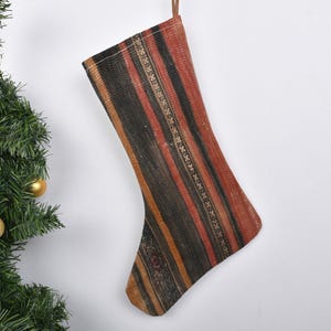 May include: A striped Christmas stocking with a red, black, and gold pattern. The stocking is made of fabric and has a loop at the top for hanging.