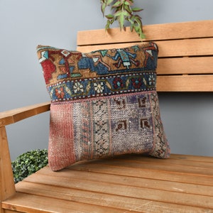 May include: A colorful patterned throw pillow with a geometric design in shades of red, blue, brown, and white. The pillow is sitting on a wooden bench.